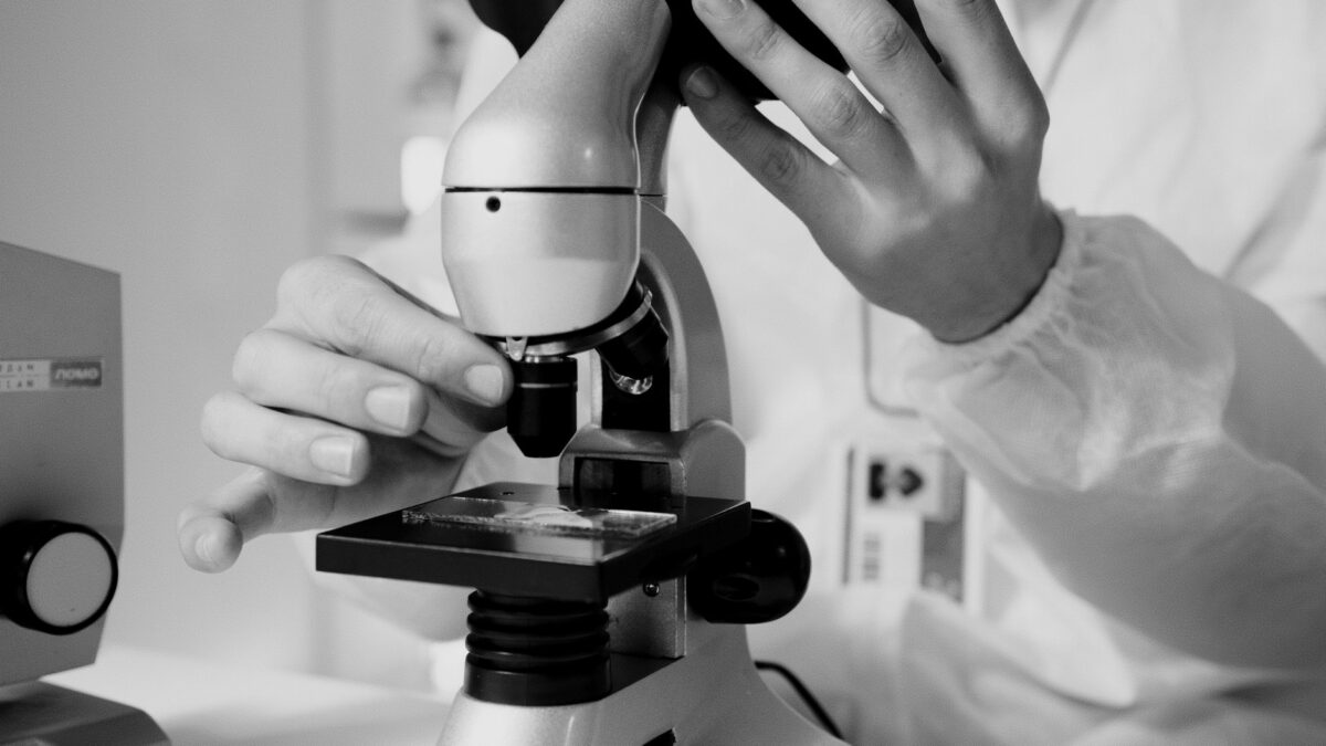 A scientist in a lab coat using a microscope for research in a laboratory setting.