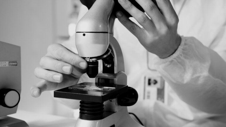 A scientist in a lab coat using a microscope for research in a laboratory setting.